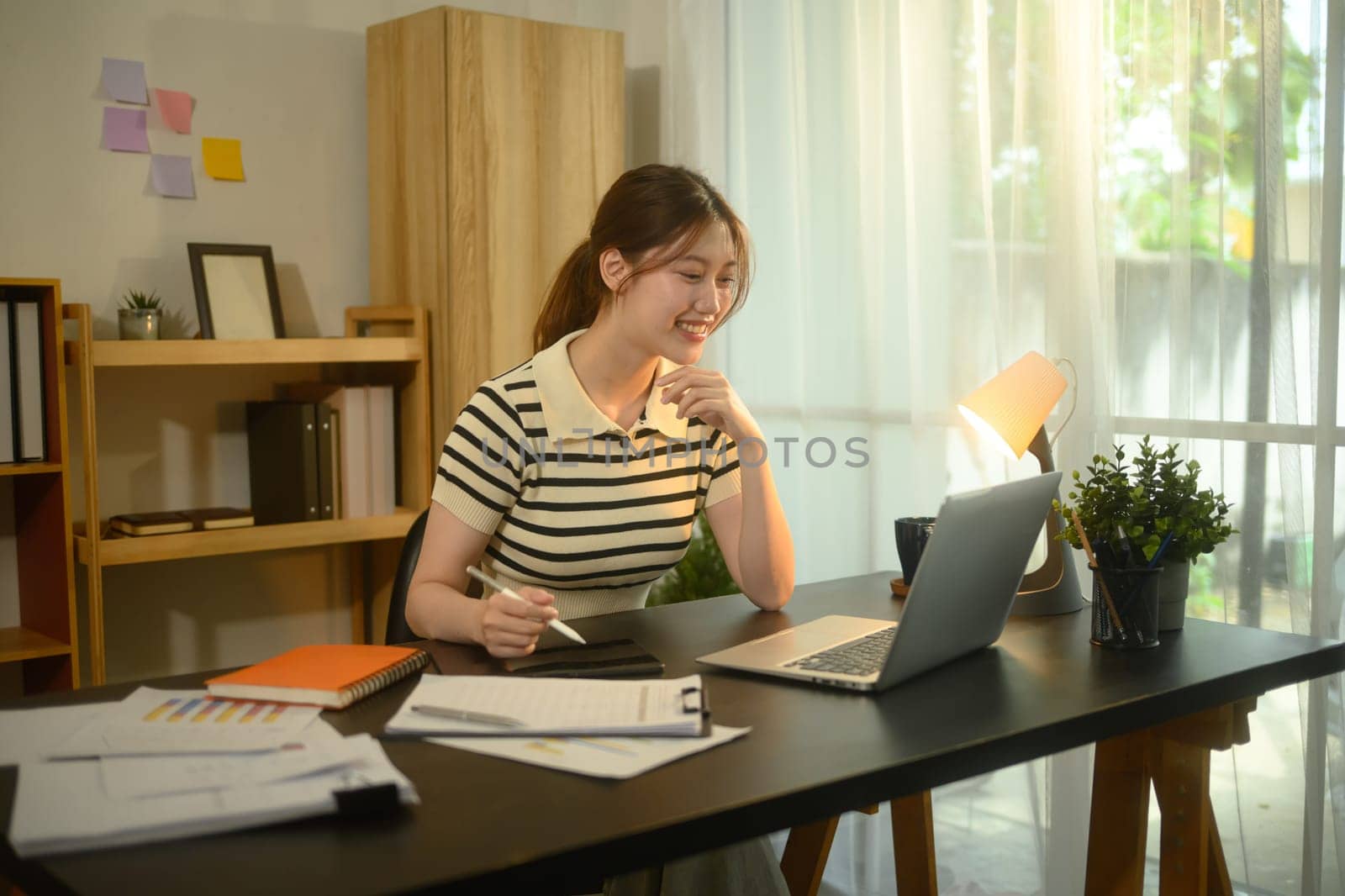 Smiling woman working in a bright home office with laptop and documents.