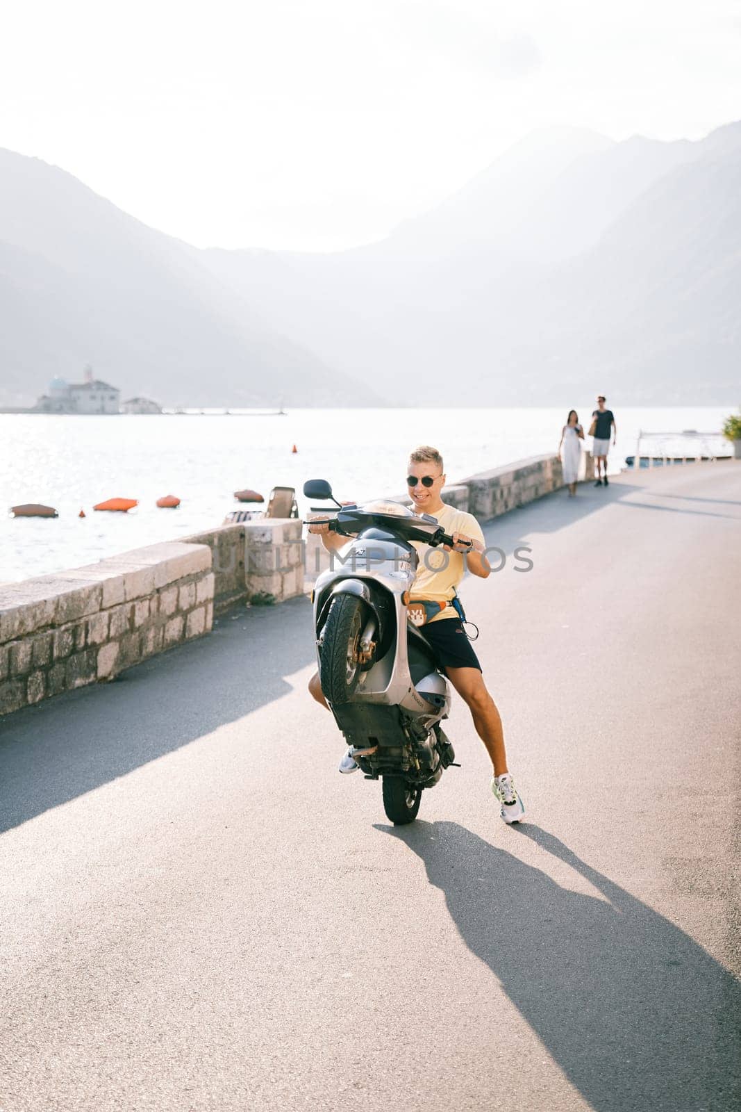 Smiling young man lifted a motor scooter onto the rear wheel while sitting on the seat. High quality photo