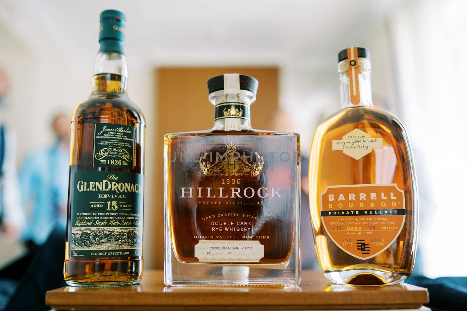 Bottles of whiskey stand on the table in front of the men. Caption: Glendronach Revival, Hillrock, Barrell Bourbon. High quality photo