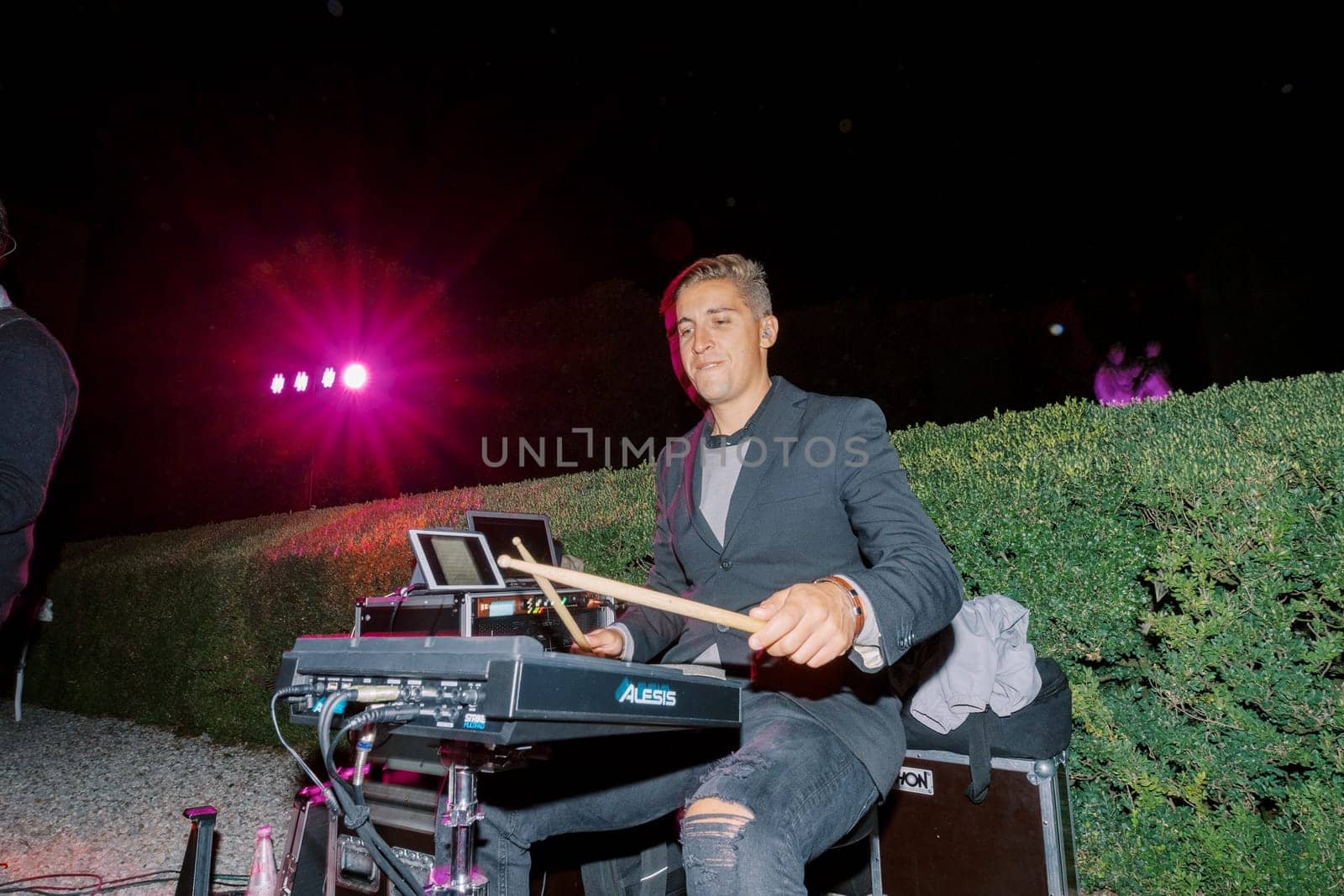 Drummer with sticks sitting at a modern electronic drum kit in the garden. High quality photo