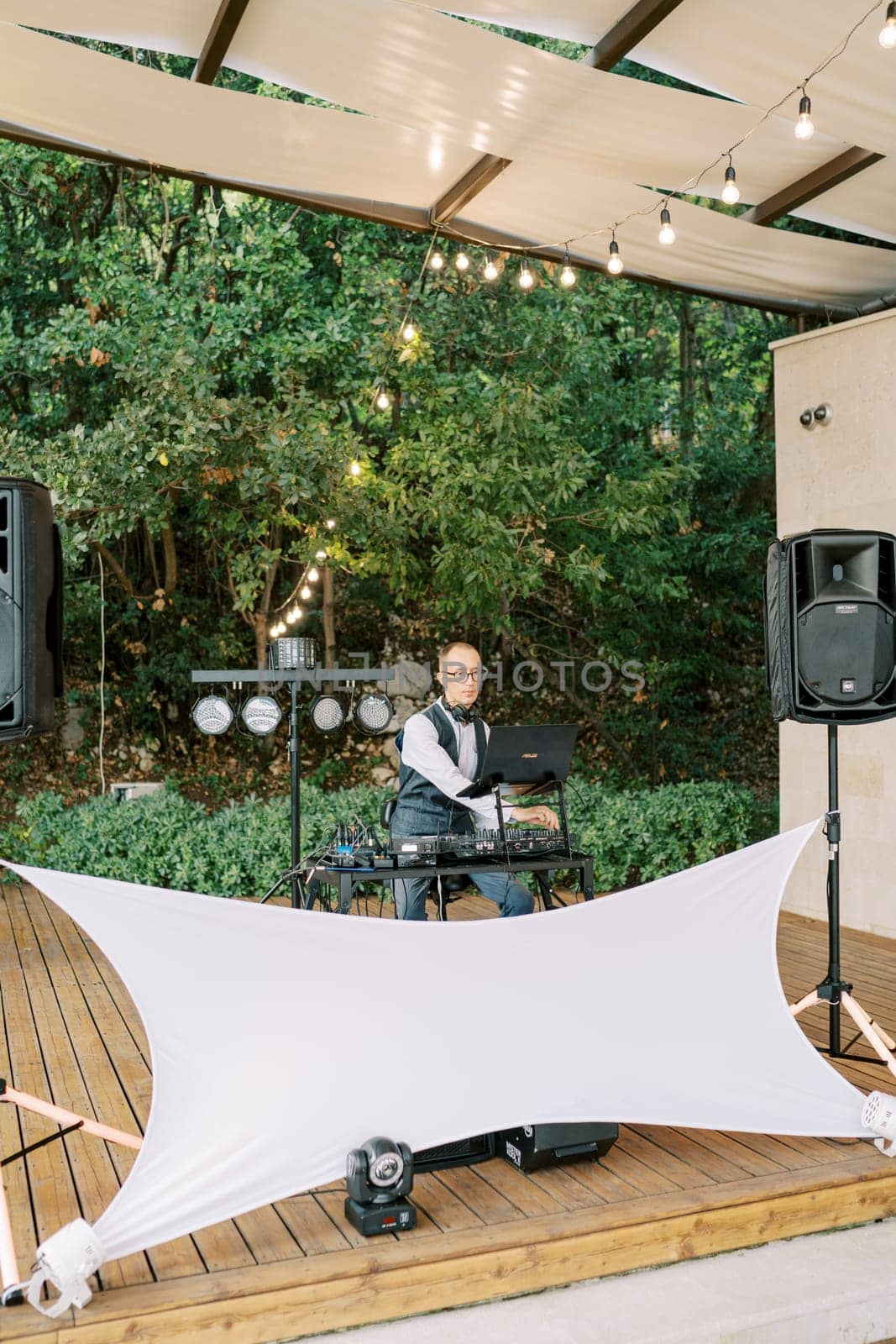 DJ sits on a chair at the console on a stage under cover in the garden. High quality photo