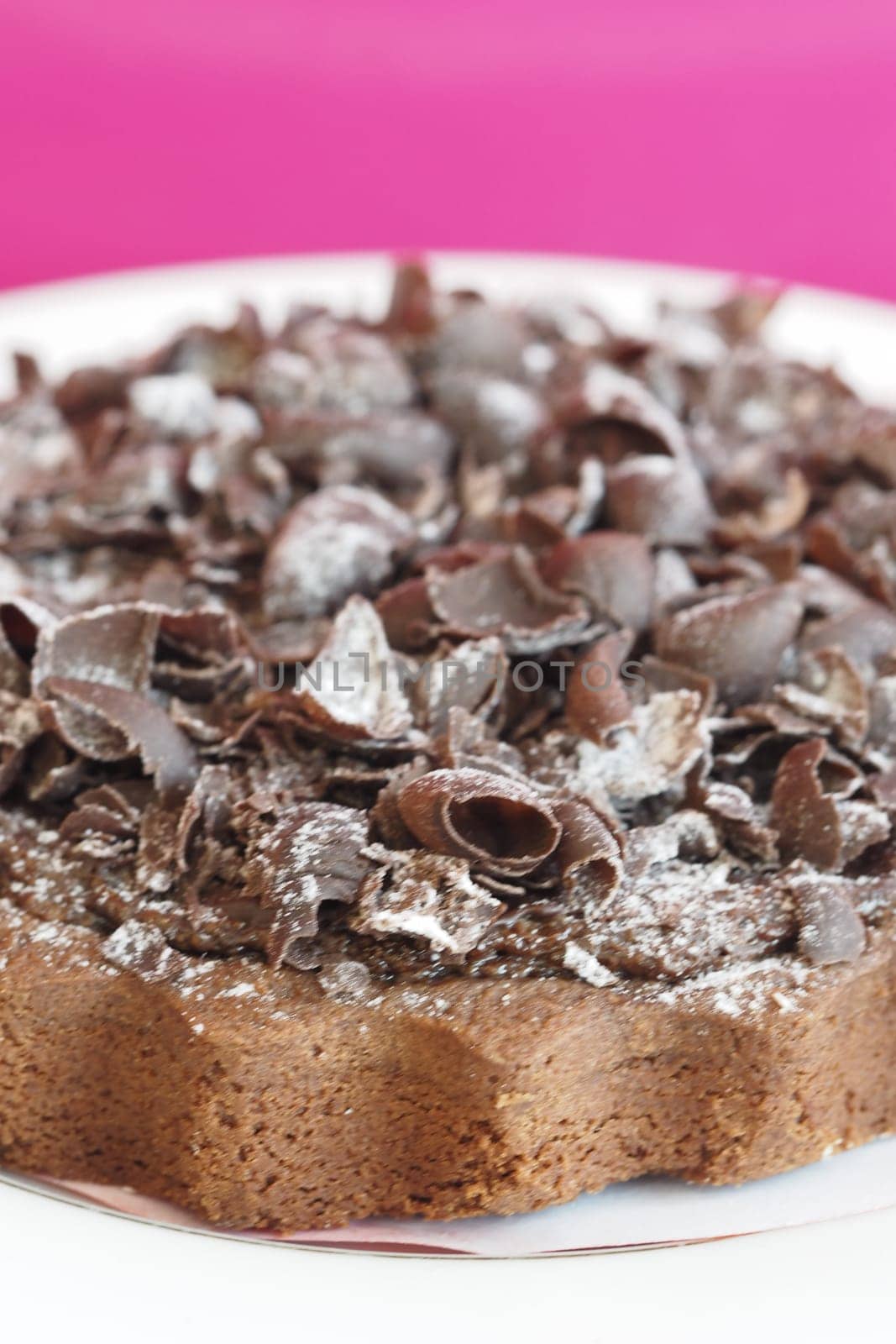 A rich chocolate dessert adorned with chocolate shavings on a bright plate.