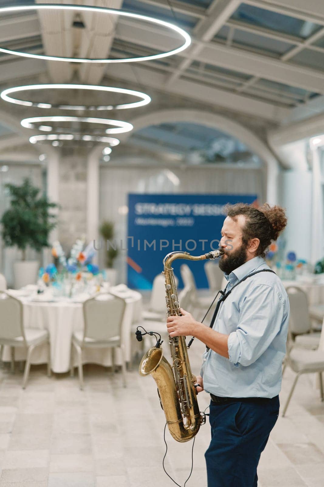 Saxophonist plays the saxophone in a restaurant near the set tables. High quality photo