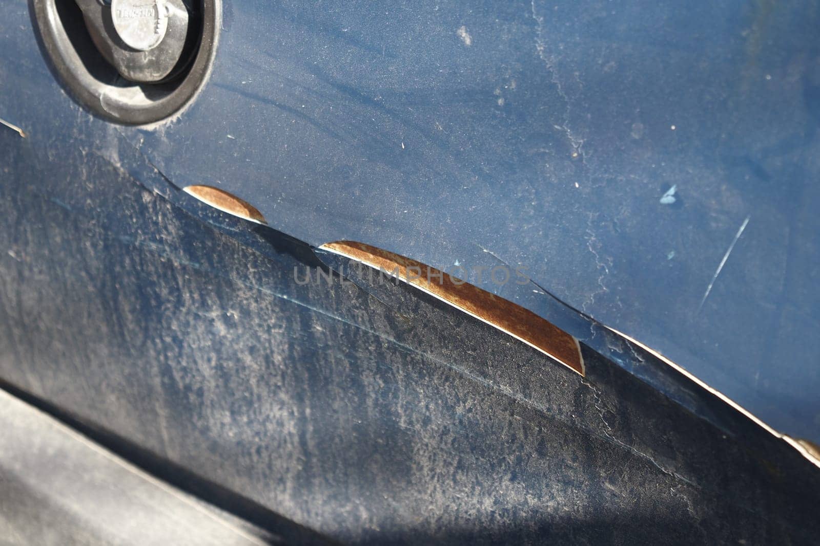 A close view of scratched car paint shows exposed metal and dirt.