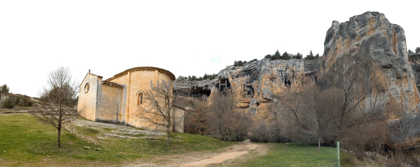 A medieval stone church lies under towering cliffs and winter trees, embodying the serene beauty of the historic landscape.