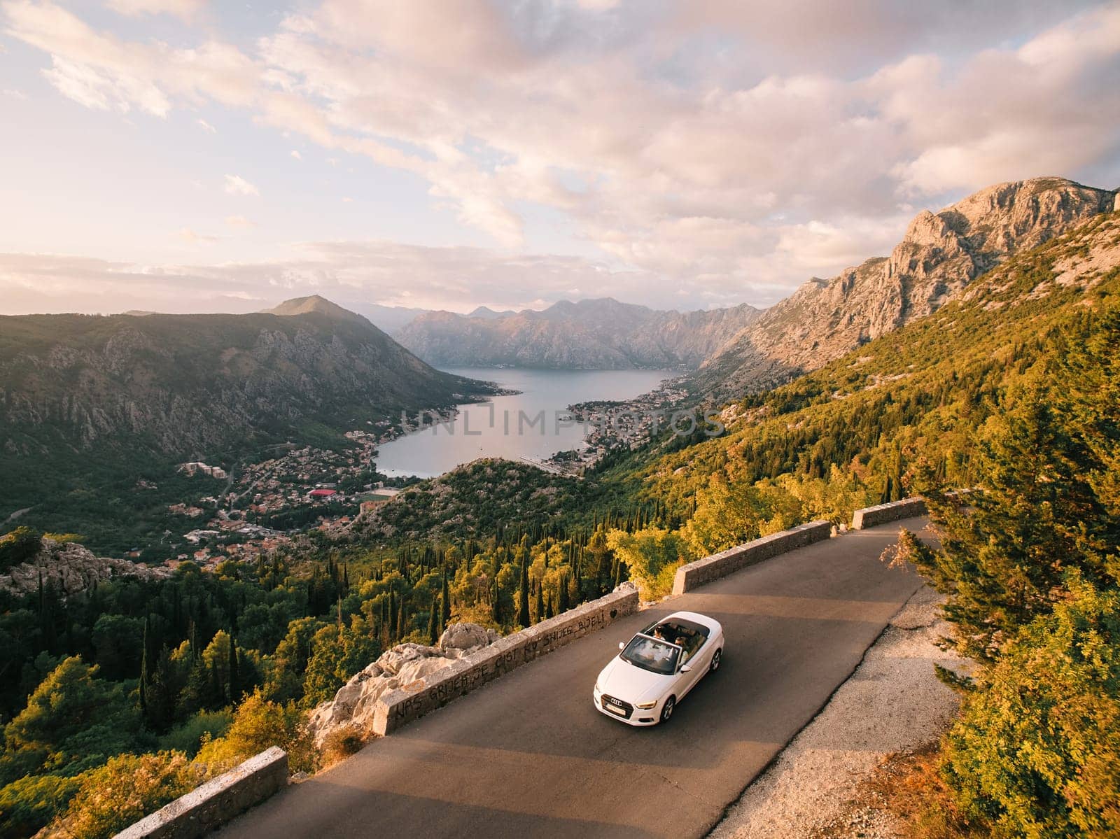 Bride and groom are driving in a white convertible along a road in the mountains above the Bay of Kotor. Montenegro. Drone. High quality photo