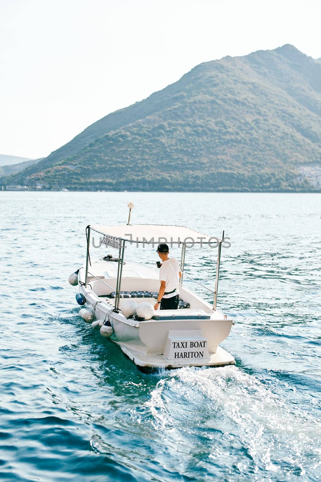 White boat with a canopy floats on the sea. Caption: Taxi boat Hariton. High quality photo