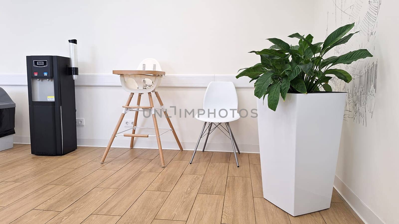 Modern waiting room with high chair, white chair, and potted plant.