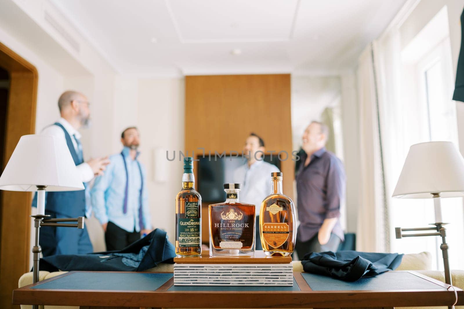 Three bottles of expensive whiskey stand on the table against the backdrop of laughing men. High quality photo
