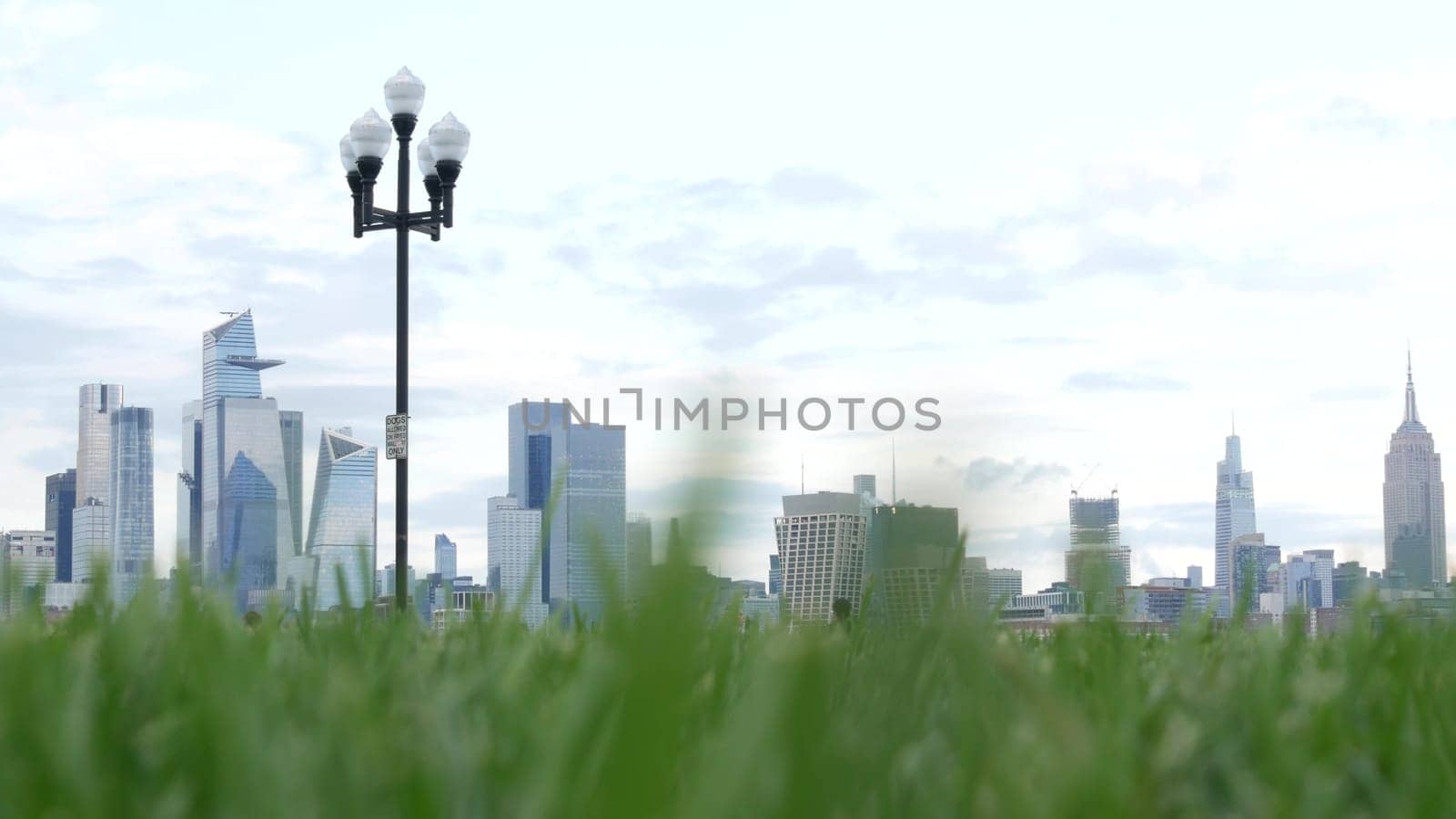 New York City, United States - 11 Sept 2023: Waterfront skyline, Manhattan Midtown Hudson Yards, riverfront skyscrapers. Waterside cityscape from Pier A Park, Hoboken, New Jersey. People on grass lawn