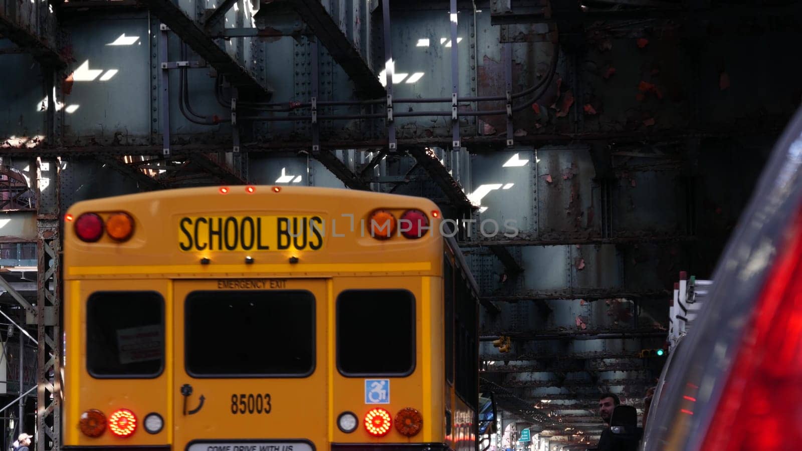 New York City, United States - 7 Sept 2023: Elevated subway above street. Metropolitan bridge over road, Queens. Overhead metro line. Car under railway track. Urban life. Yellow school bus, education