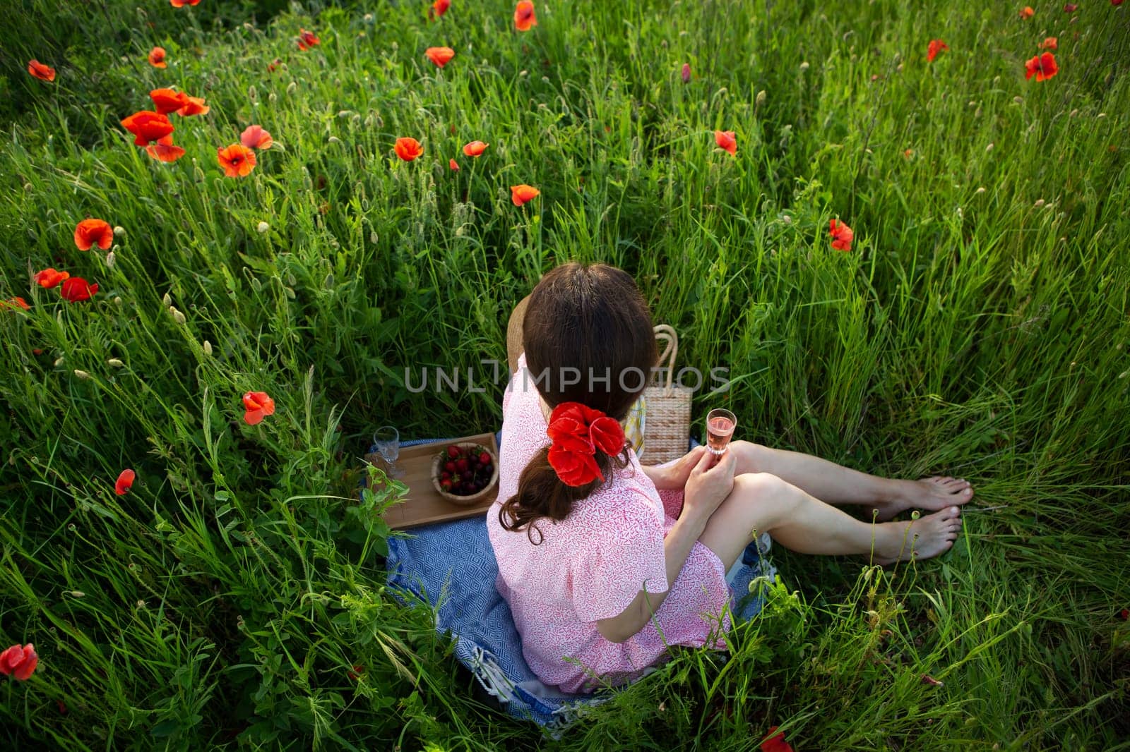 A young woman enjoys a picnic amidst a vibrant poppy field, savoring rose wine and fresh berries.