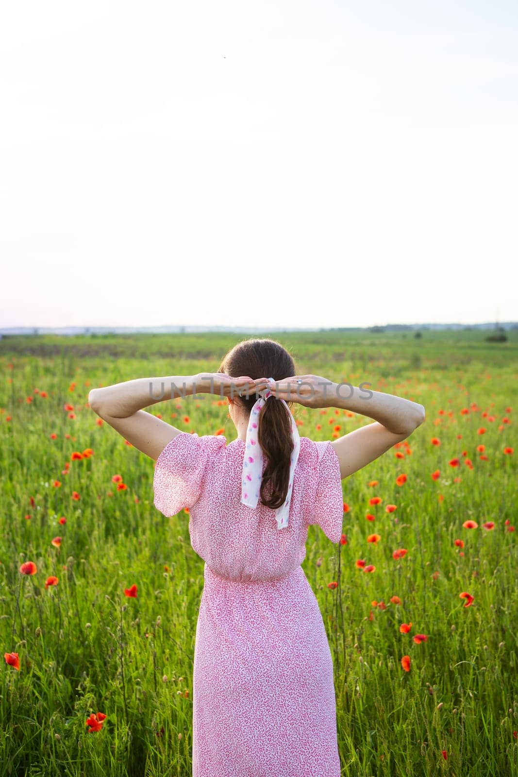 A woman in a pink floral dress enjoys a serene moment in a poppy field, her hair tied up in a silk ribbon.