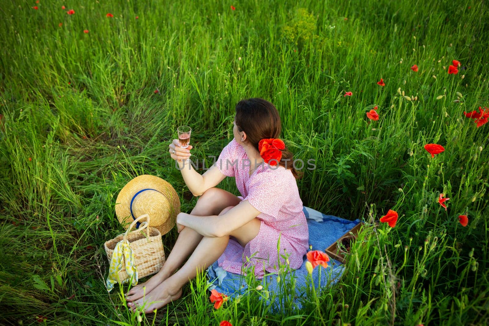 A woman enjoys a picnic in a vibrant poppy field, raising a glass of rose wine.