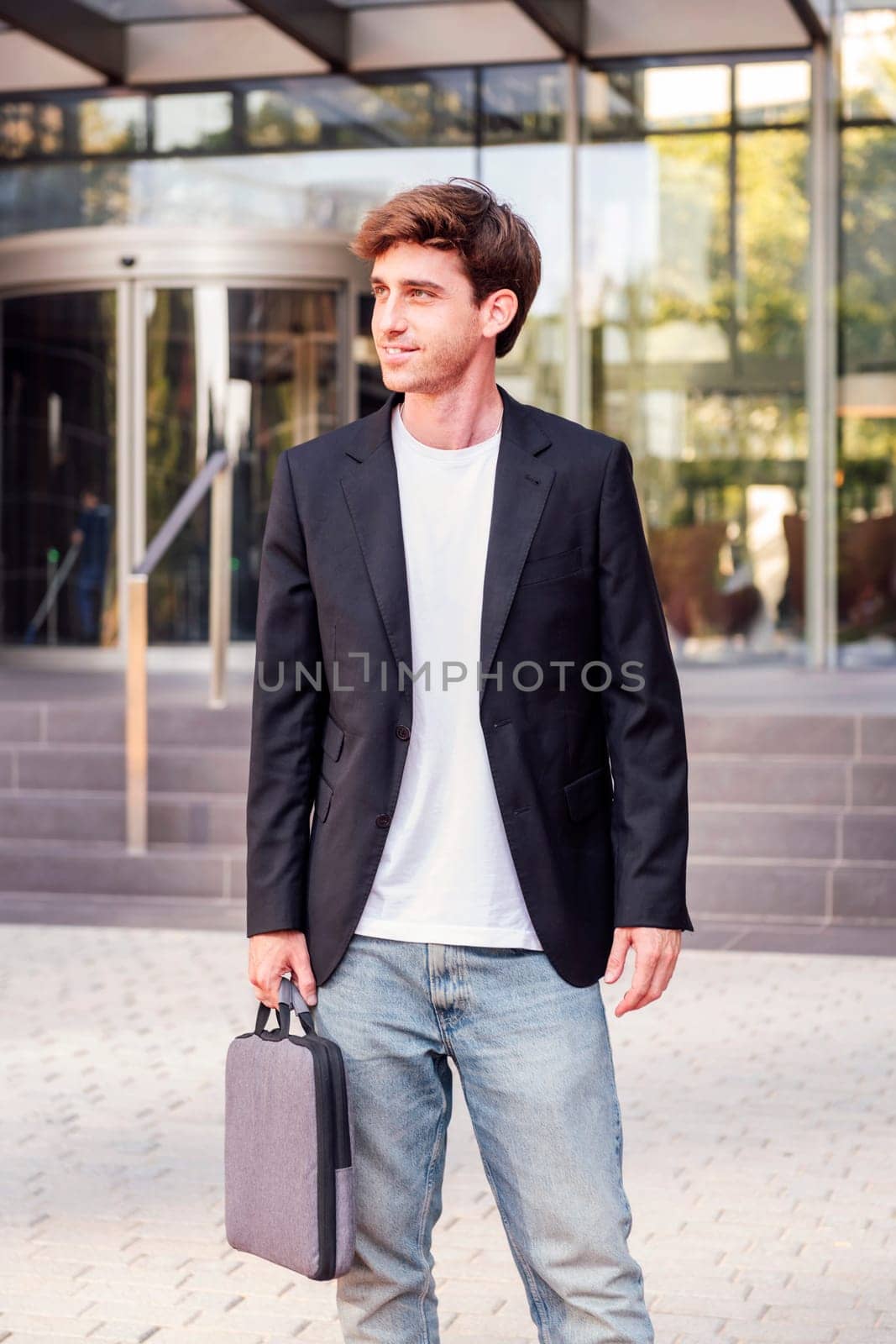 young adult man in casual suit standing holding a briefcase in front of an office building, concept of entrepreneur and business