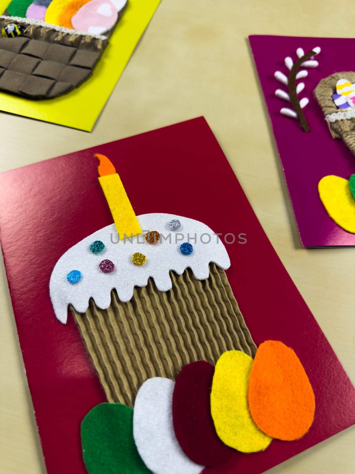 Whimsical handmade Easter card features decorated cake with candle, complemented by colorful felt eggs. Perfect for adding joyful touch to Easter celebrations and sending heartfelt wishes