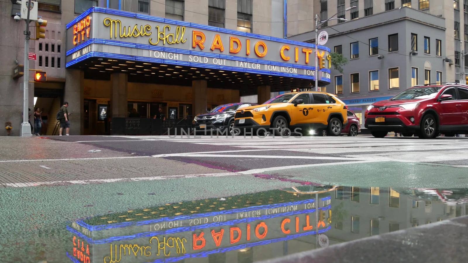 New York, United States - 10 Sept 2023: Manhattan Midtown street. Radio City Music Hall, Rockefeller Center, USA. People pedestrian, urban traffic, 6 Sixth Americas avenue crossroad, yellow taxi cab.