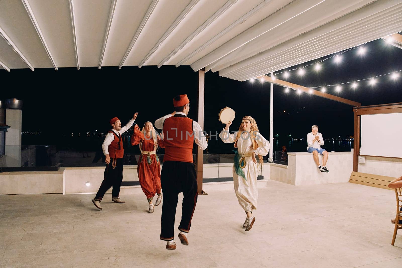 Group of men and women in national costumes dance with a tambourine on stage. High quality photo