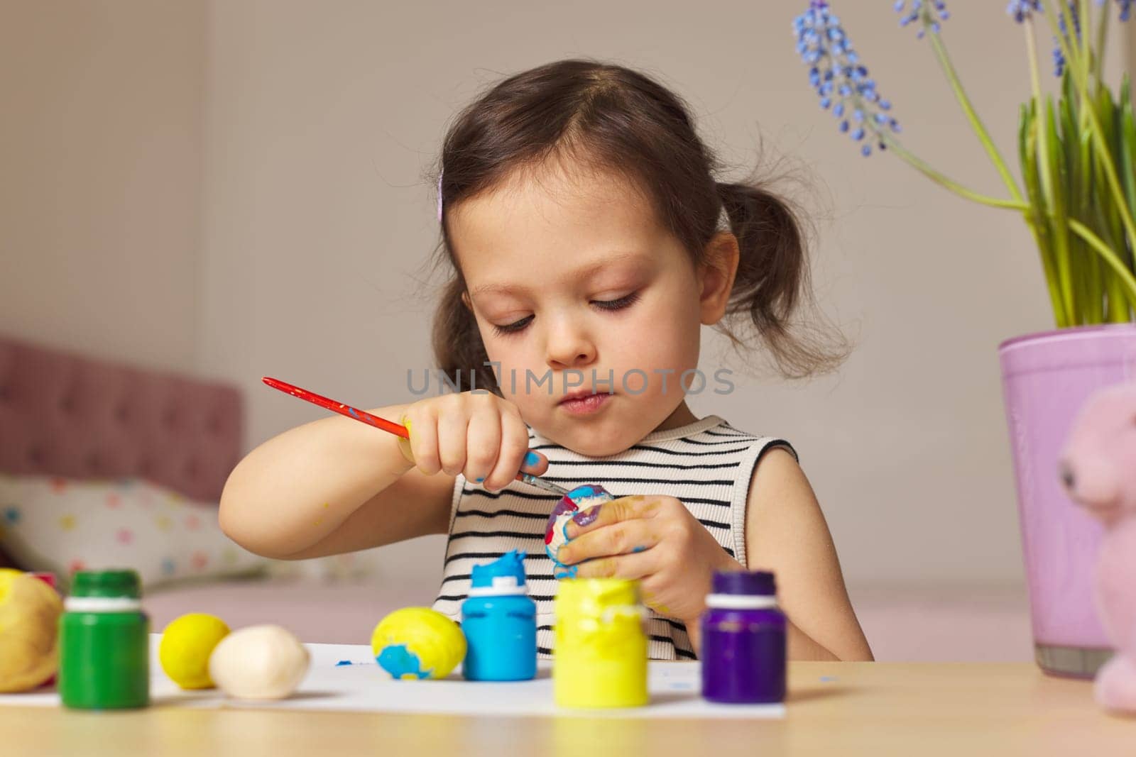 Little child girl paint Easter eggs at home. kid is preparing for Easter.