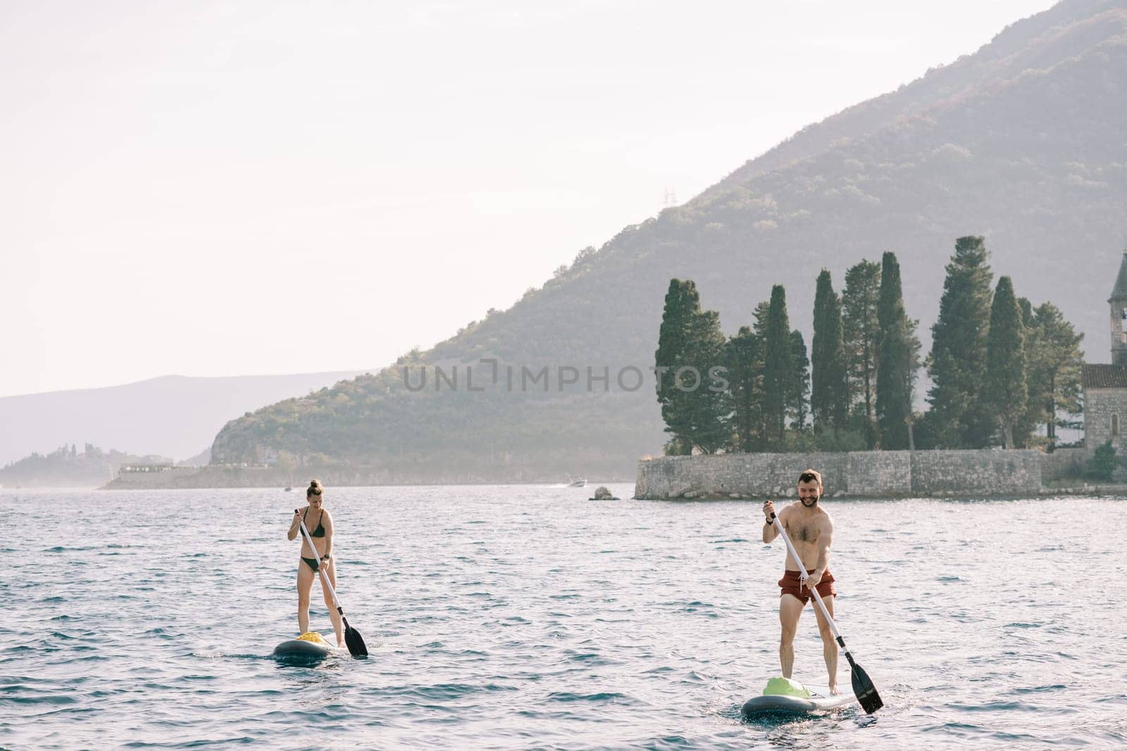 SUP surfers float on boards using oars along the Bay of Kotor. Montenegro. High quality photo