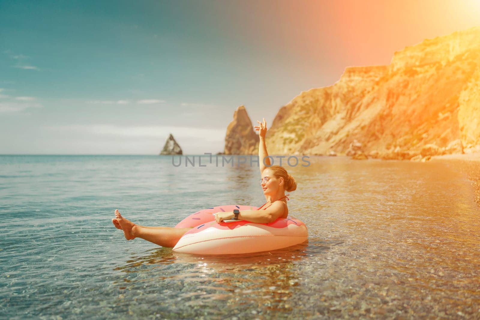 Woman laptop sea. Freelancer woman in sunglases floating on an inflatable big pink donut with a laptop in the sea. People summer vacation rest lifestyle concept