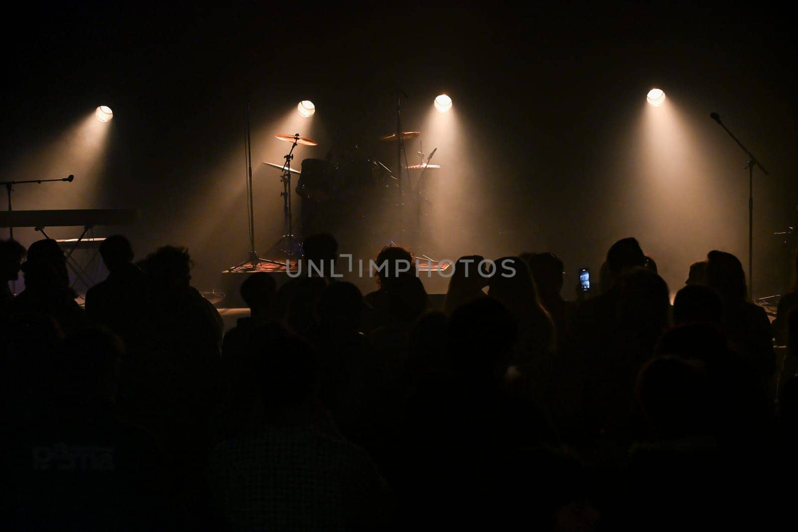 Audience gathers in a lively venue, eagerly anticipating the performance as stage lights illuminate the setup, creating a vibrant atmosphere filled with excitement and energy.