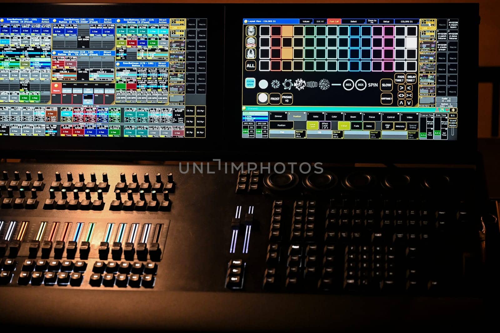 A detailed view of a lighting control panel featuring multiple digital displays and buttons, actively being used during a rehearsal at a theater venue.