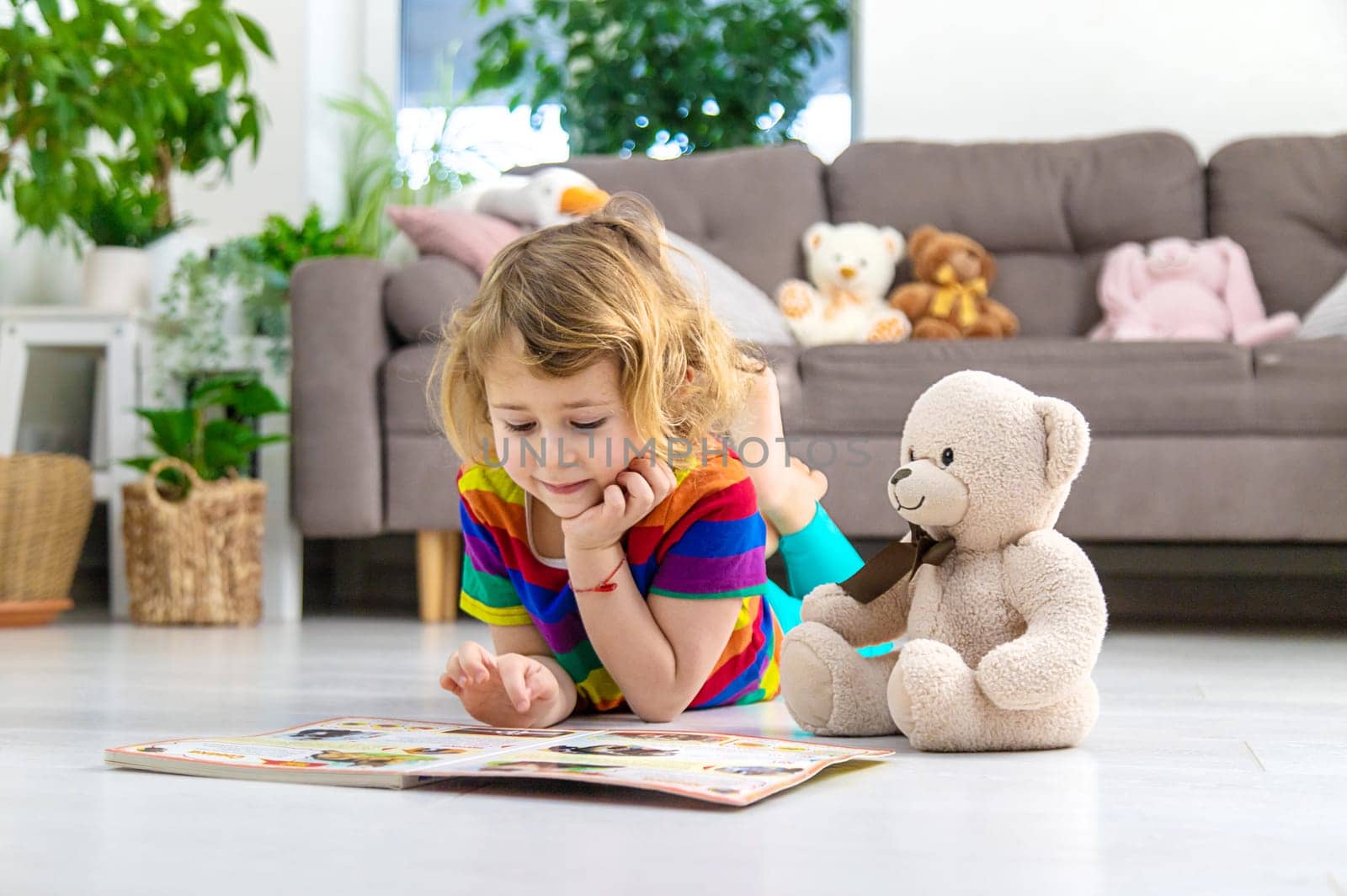 Child reading a book at home with a teddy bear at home. Selective focus. kid.