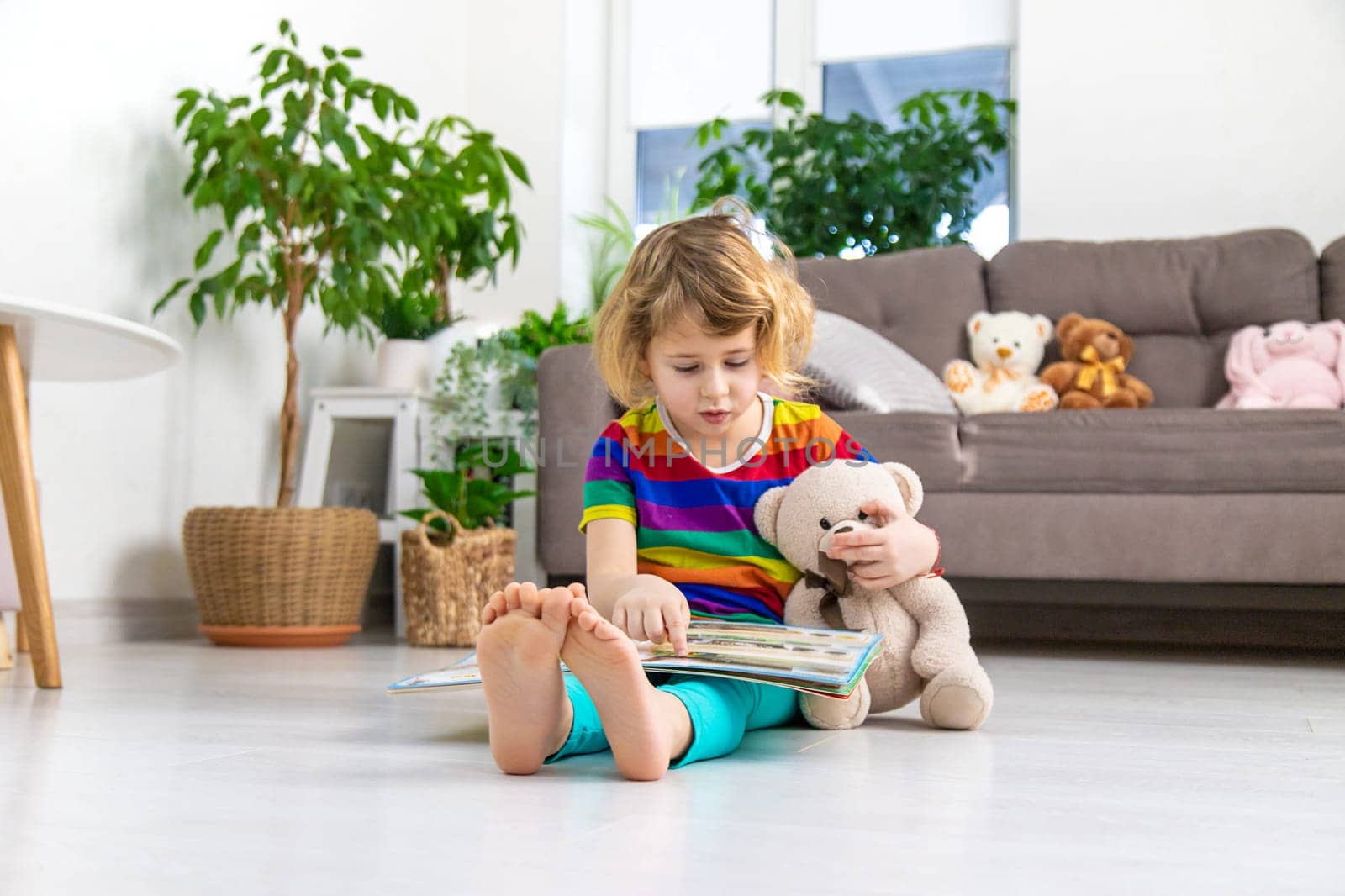 Child reading a book at home with a teddy bear at home. Selective focus. kid.