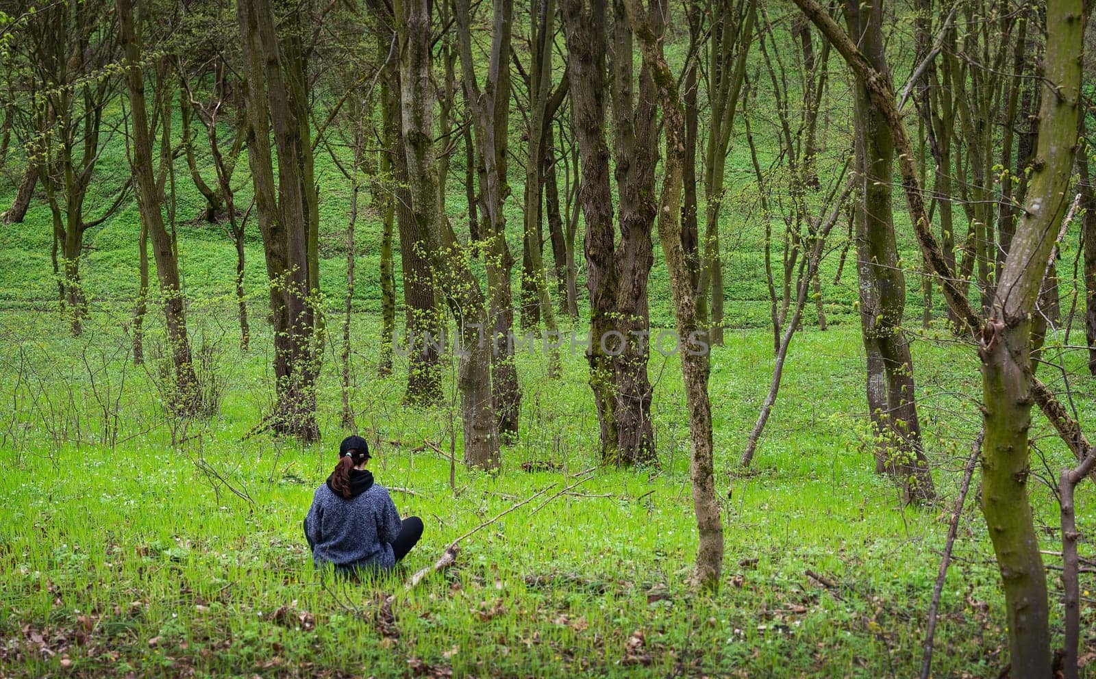 A woman sits serenely in a sun-dappled spring forest, enjoying the tranquil atmosphere.