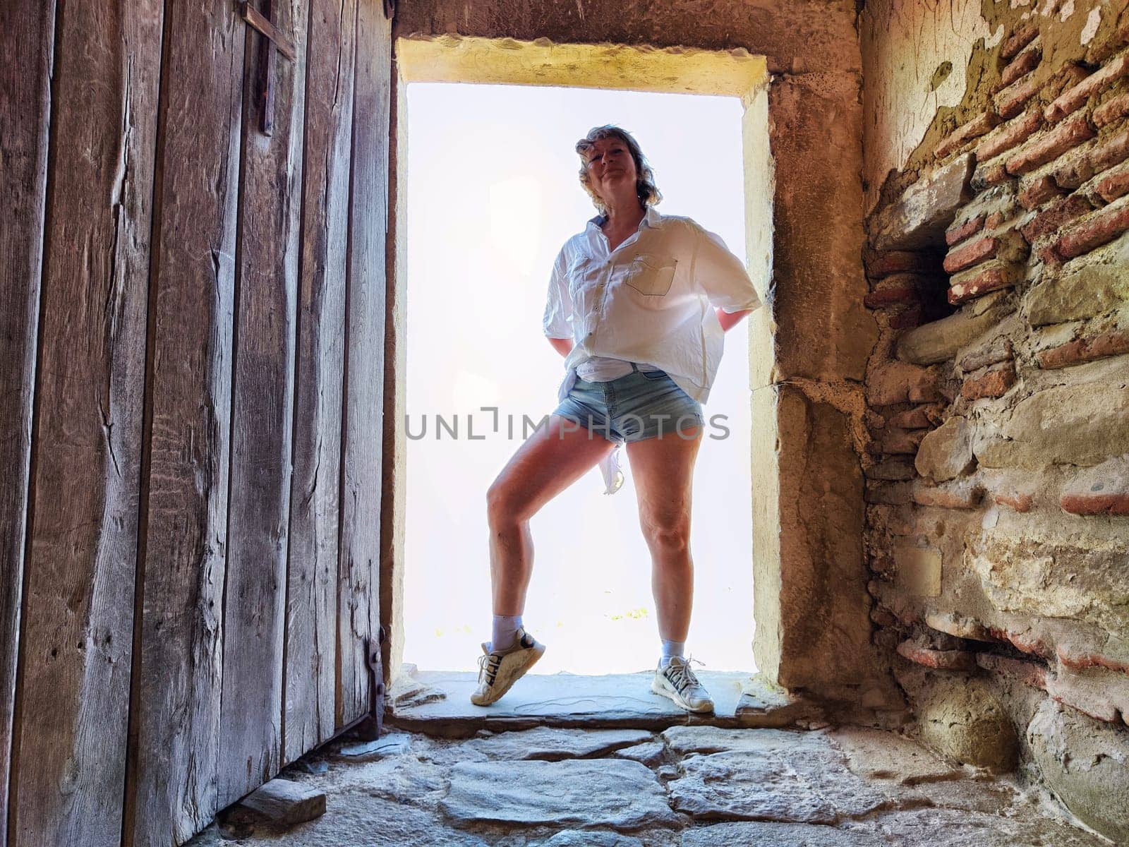 A 50-year-old woman poses playfully in a doorway while on a travel adventure, embracing her lifestyle as a blogger.