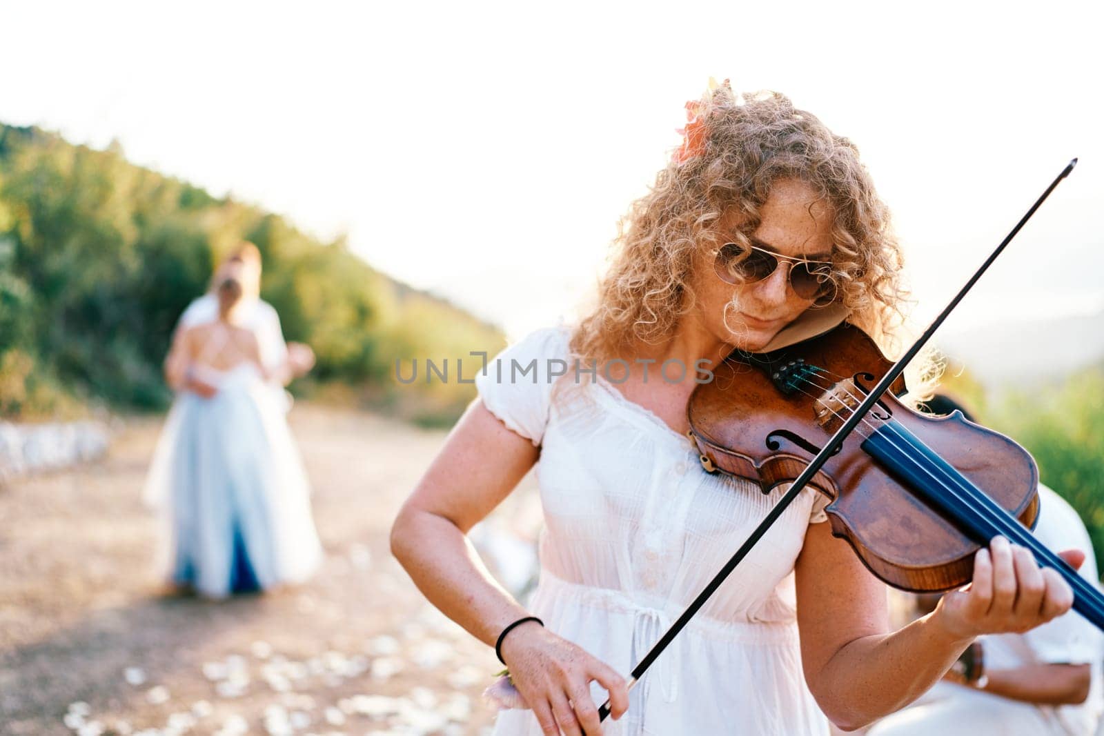 Violinist plays the violin in a clearing with bride and groom dancing in the background. High quality photo