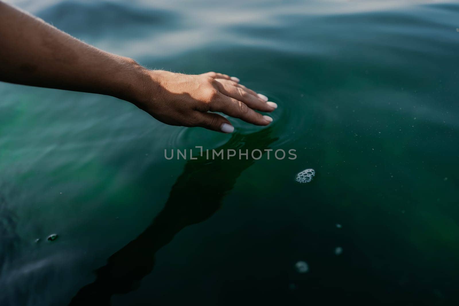 The hand touches the water, creating ripples. The water is calm and clear, and the hand is white. Concept of tranquility and peacefulness