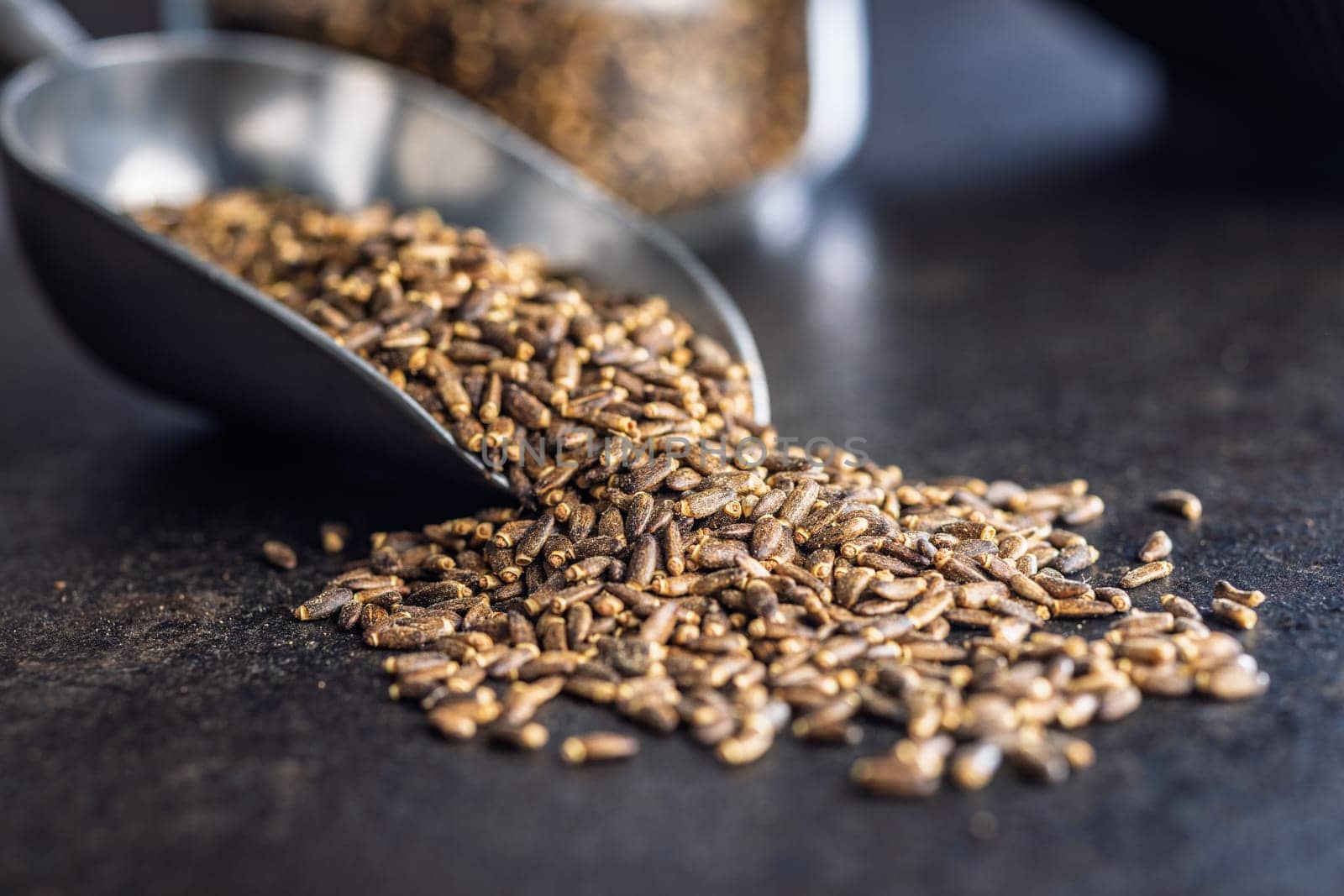 Milk thistle seeds in scoop on a black table.