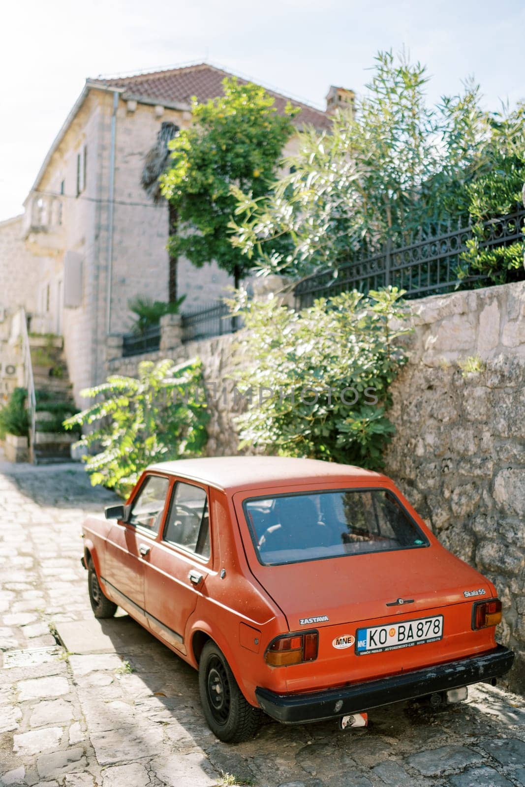 Red vintage car Zastava Skala 101 stands near the stone fence of an old house. High quality photo