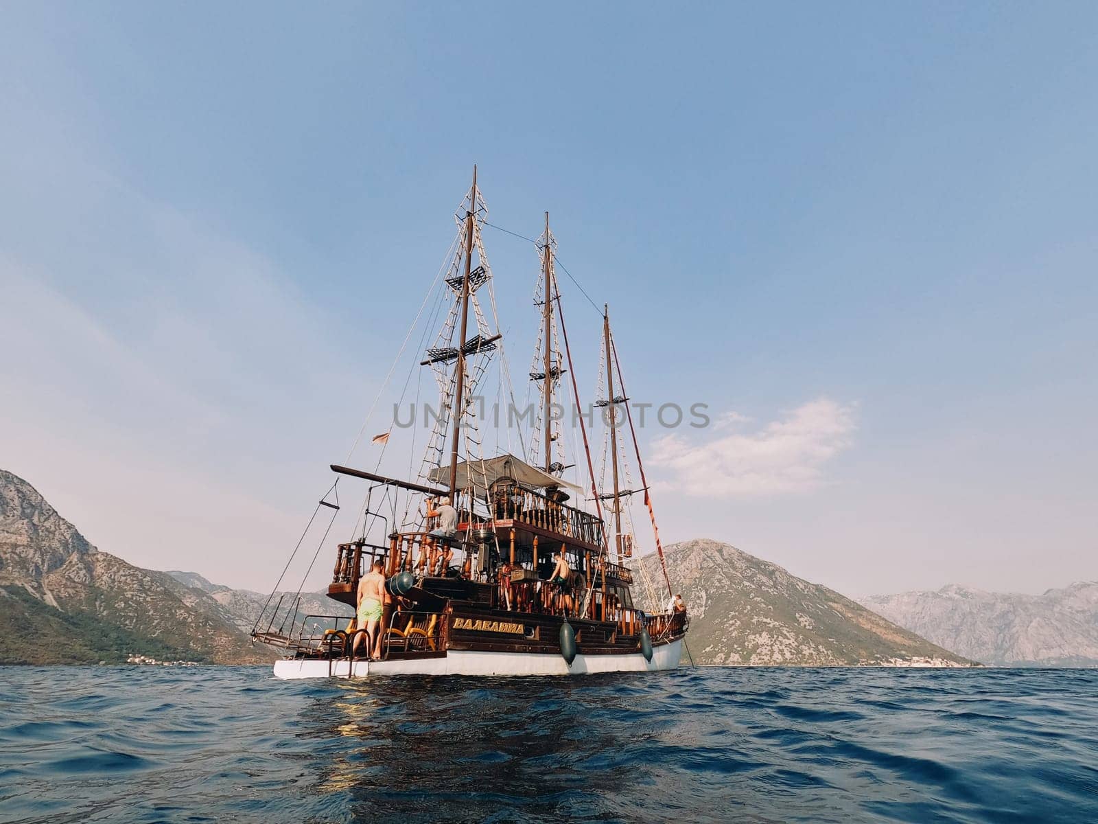 Guys in swimming trunks walk on board a wooden tourist yacht standing in the sea. High quality photo