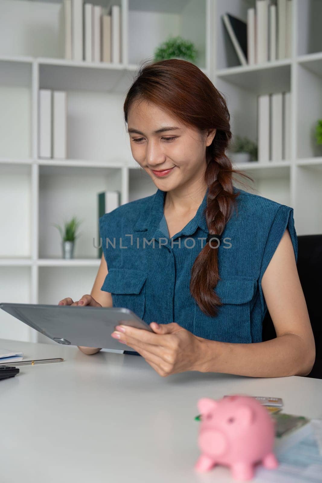 Sitting at her desk, a young woman engages with her tablet, reviewing financial insights and strategies for saving, demonstrating modern financial literacy.