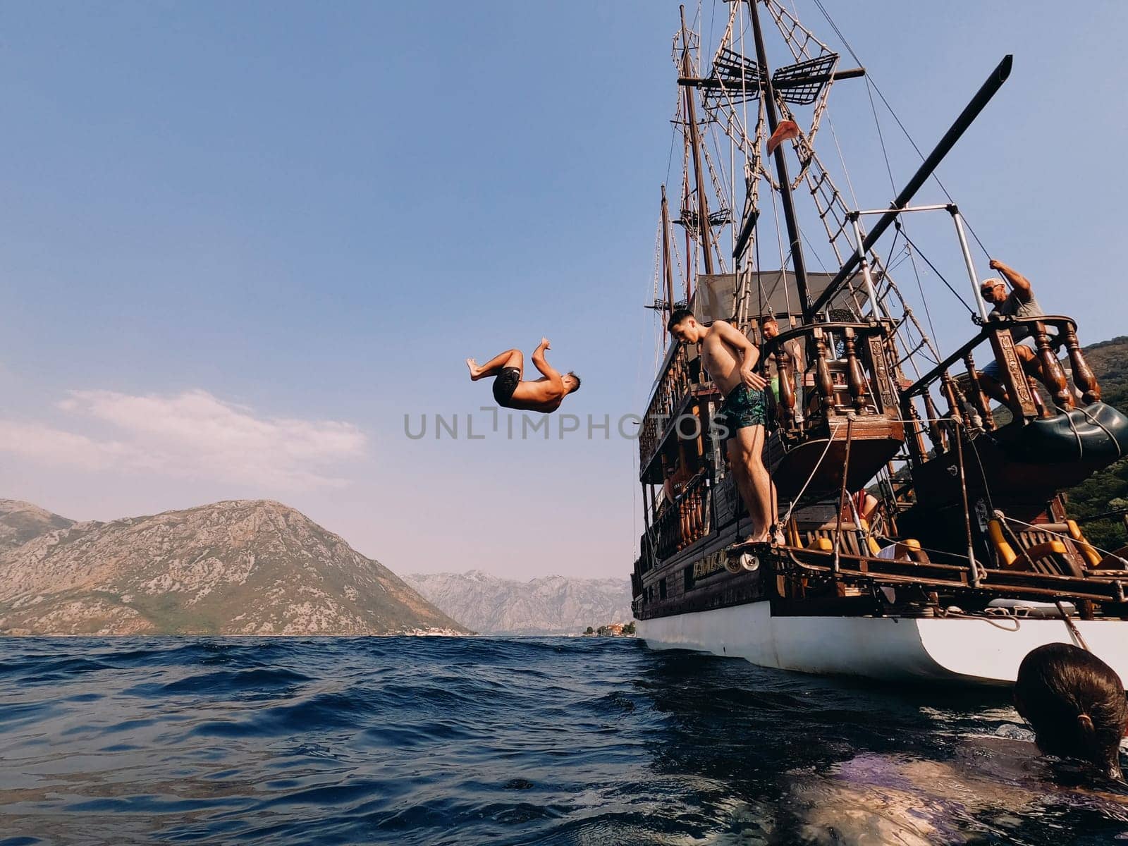 Young men jump into the sea from the deck of a wooden sailing yacht. High quality photo