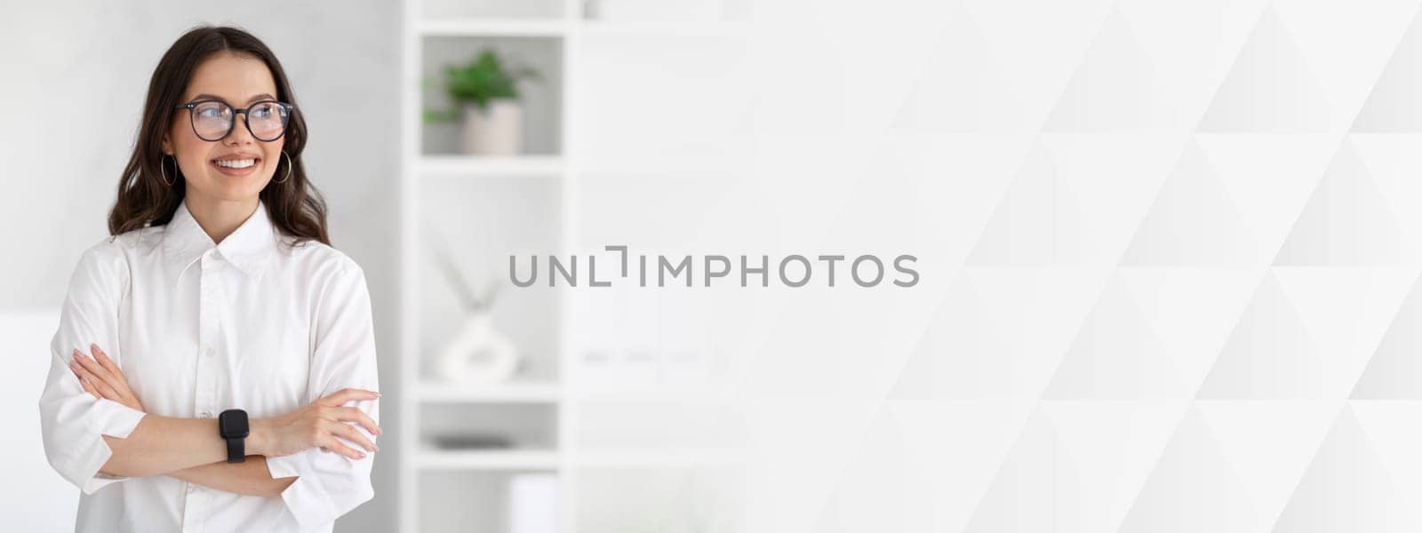 Cheerful young caucasian business woman in white shirt and glasses enjoys professional occupation, looking at copy space in office interior. Business and work, official lifestyle and ad, offer