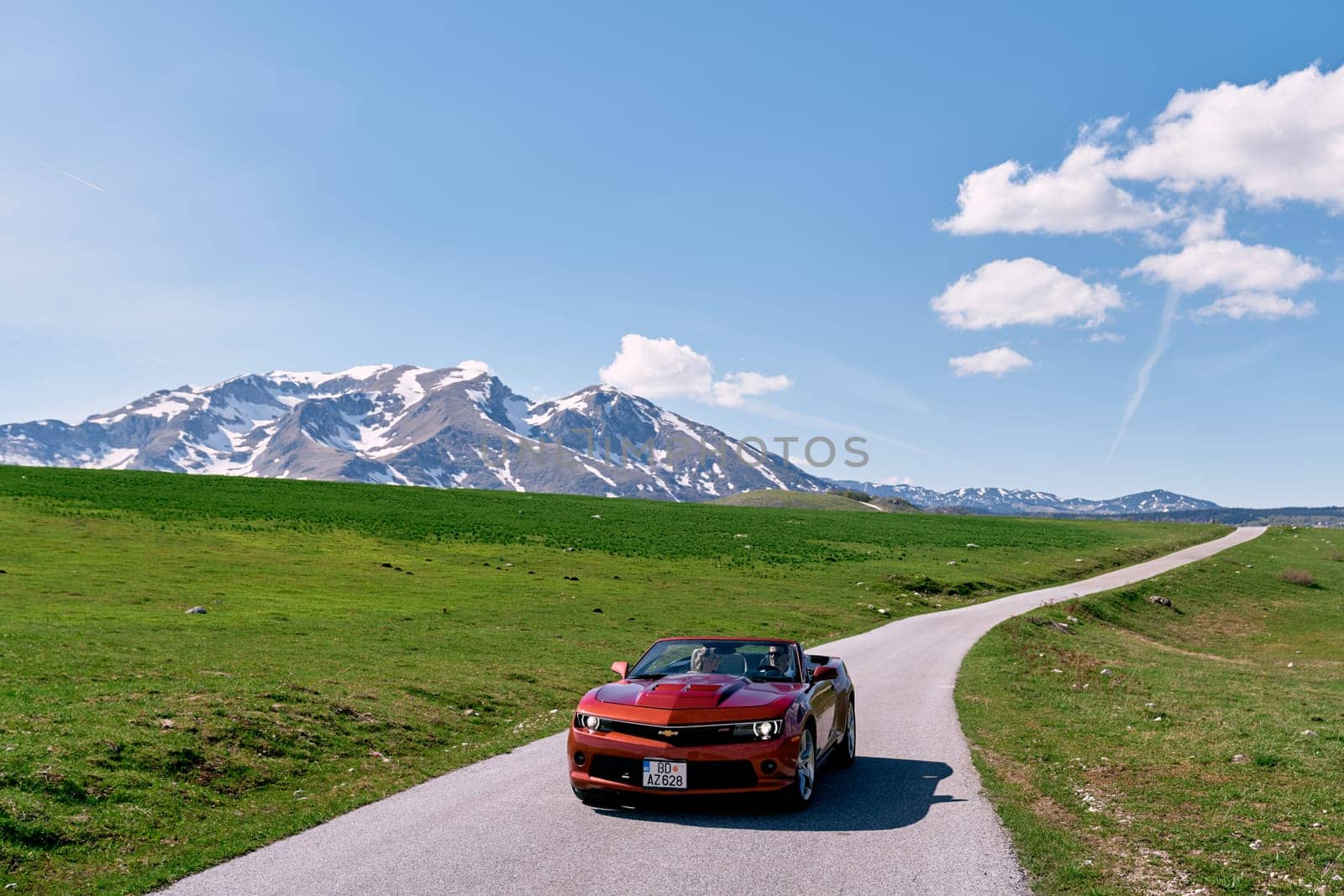 Bride and groom are driving in a red convertible along a mountain road. High quality photo