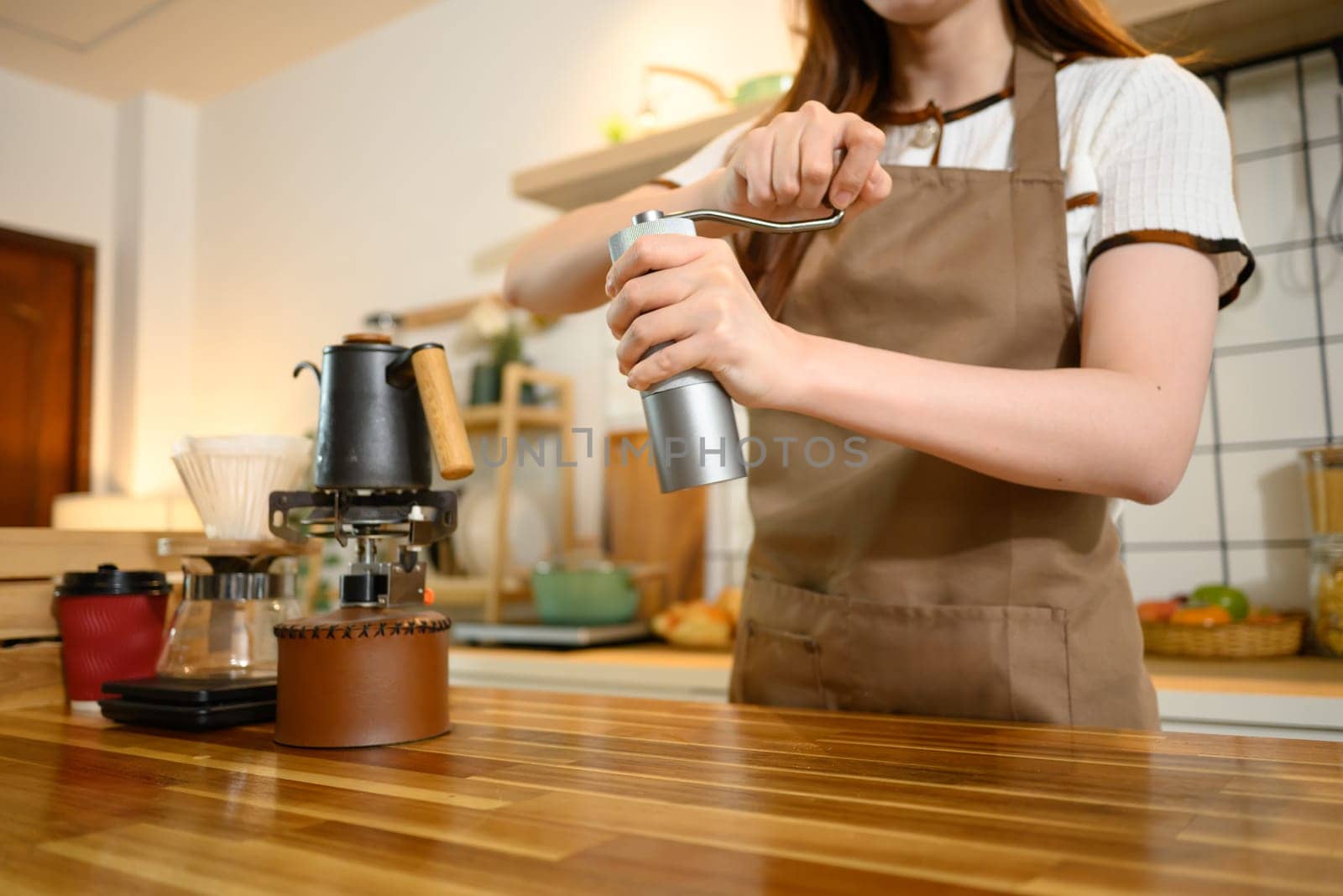 Close up of a woman using manual coffee grinder while preparing fresh coffee in a warm kitchen.