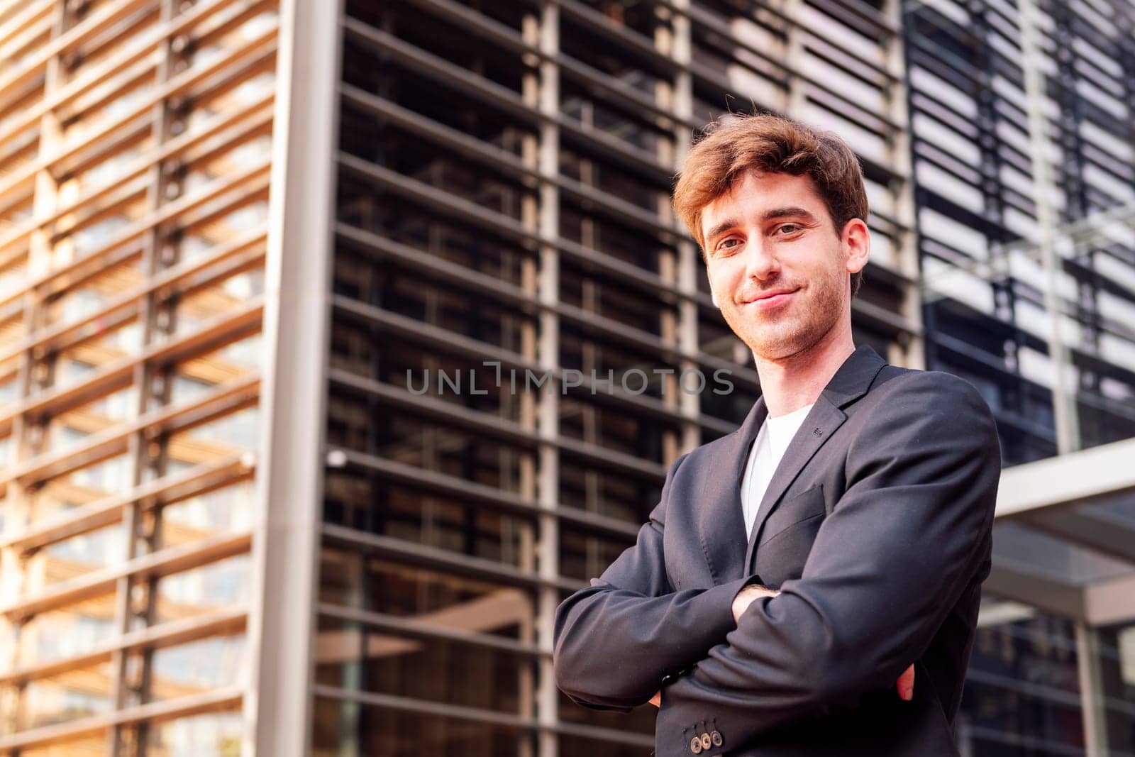 young adult man in casual suit standing looking at camera with arms crossed in front of an office building, concept of entrepreneur and business, copyspace for text