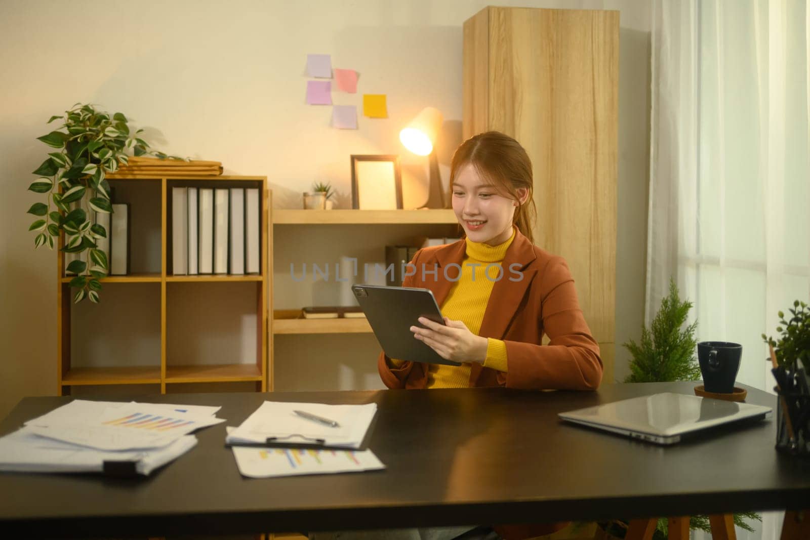 Smiling young entrepreneur wearing a brown blazer using digital tablet in stylish workplace.