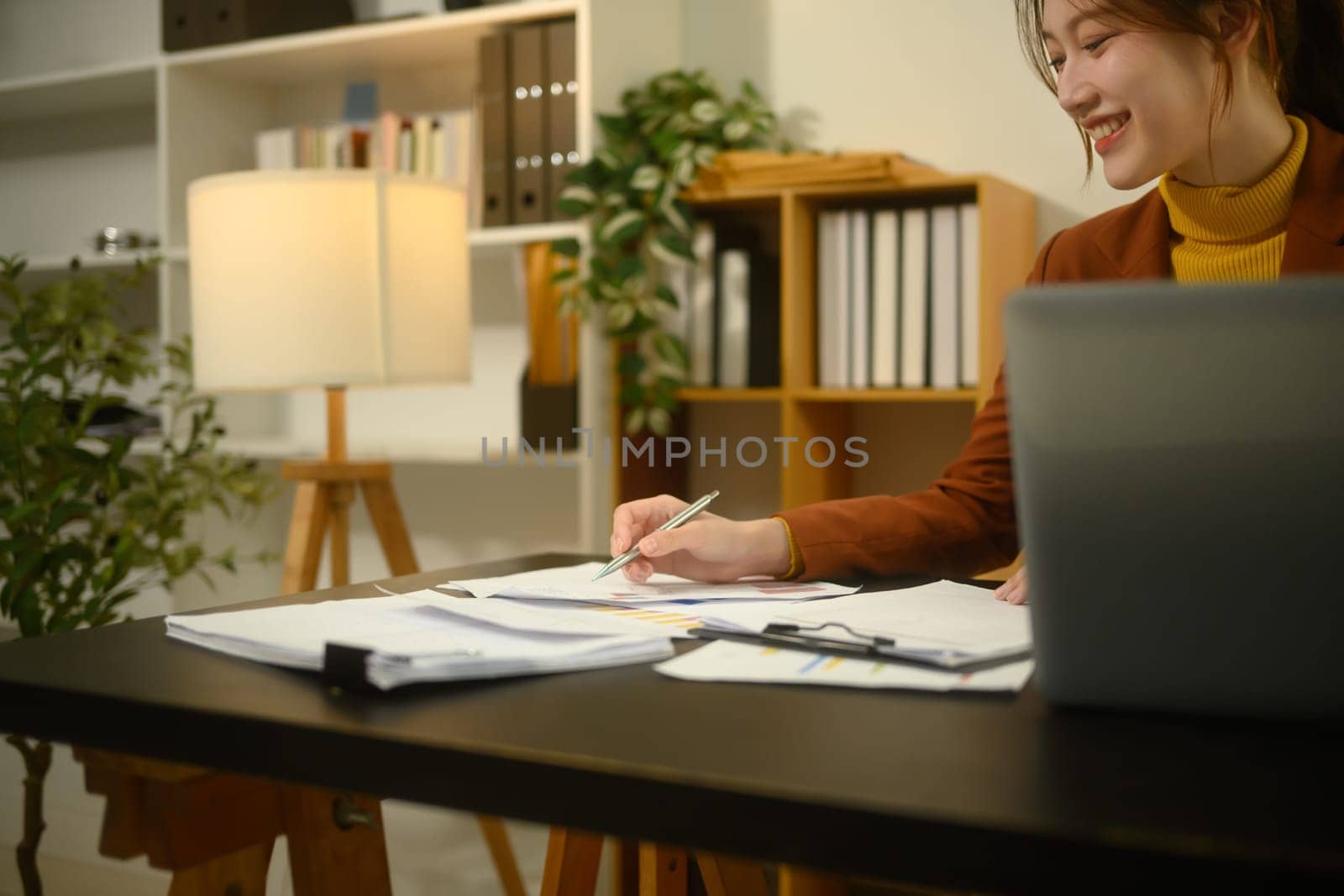 Smiling businesswoman sitting at desk with laptop, reviewing graphs and statistics.