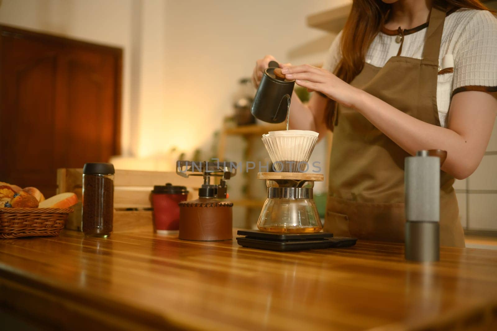 Close up of woman carefully pouring hot water into dripper to make fresh pour over coffee in a home kitchen.