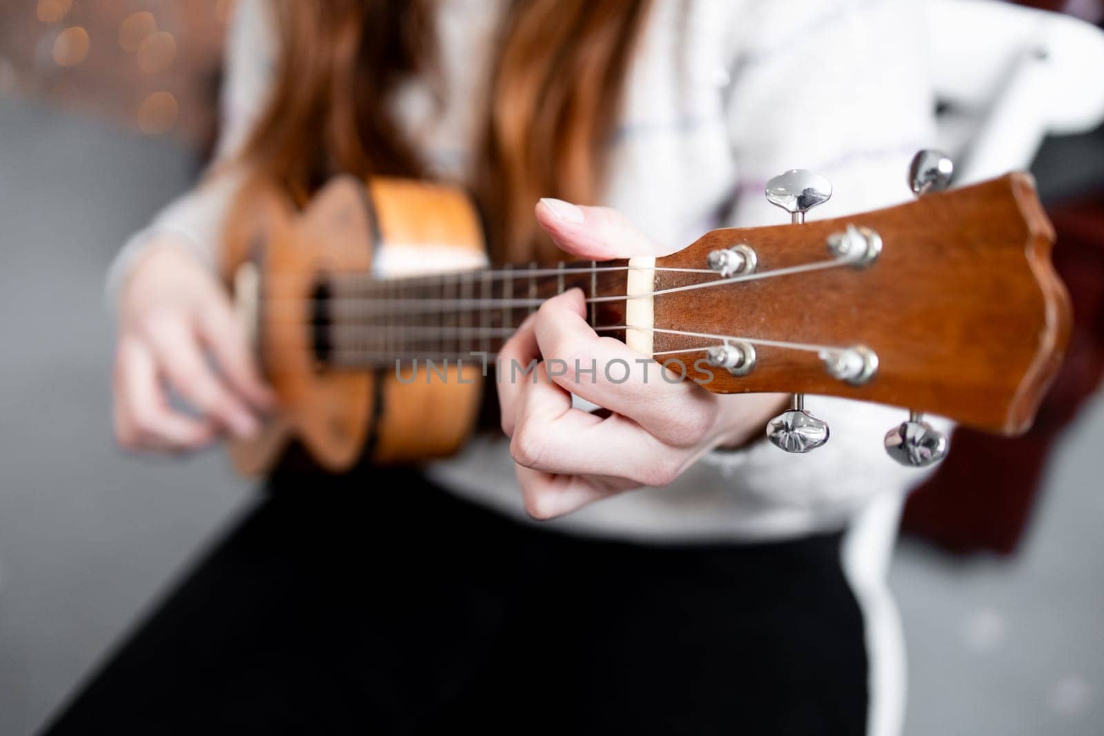 Young female playing ukulele indoors with focus on strings and hands.