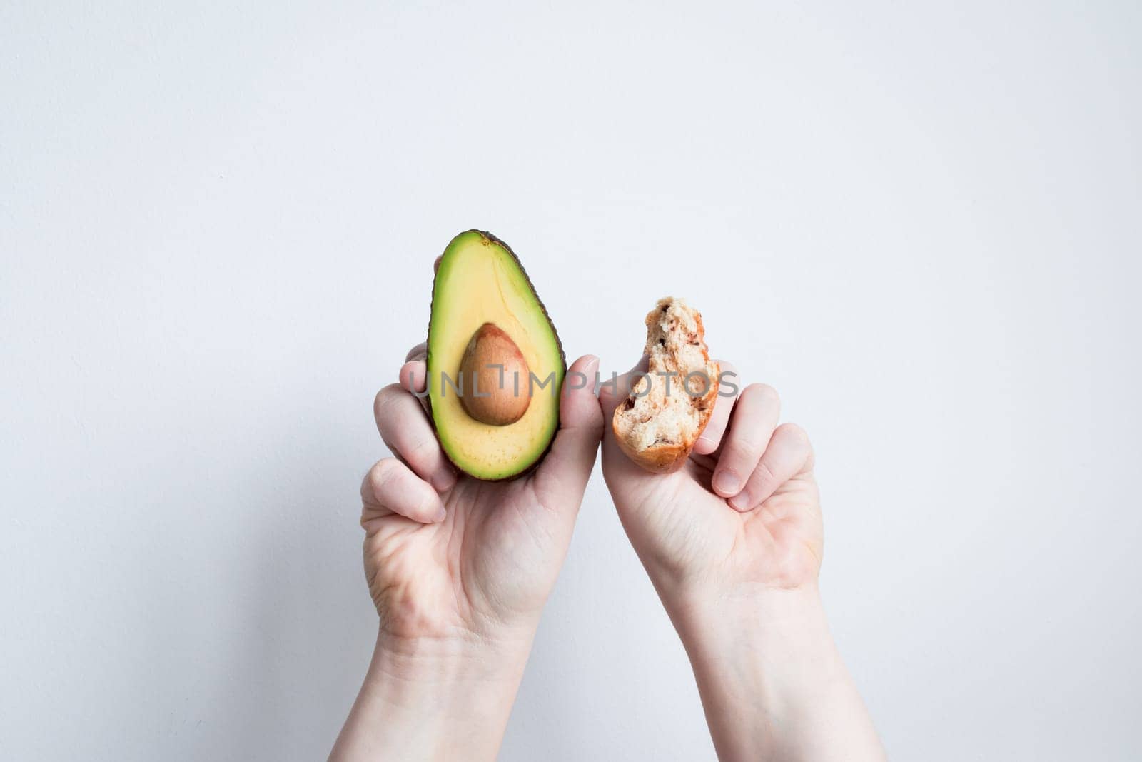 Hands holding fresh avocado and seed against white background.