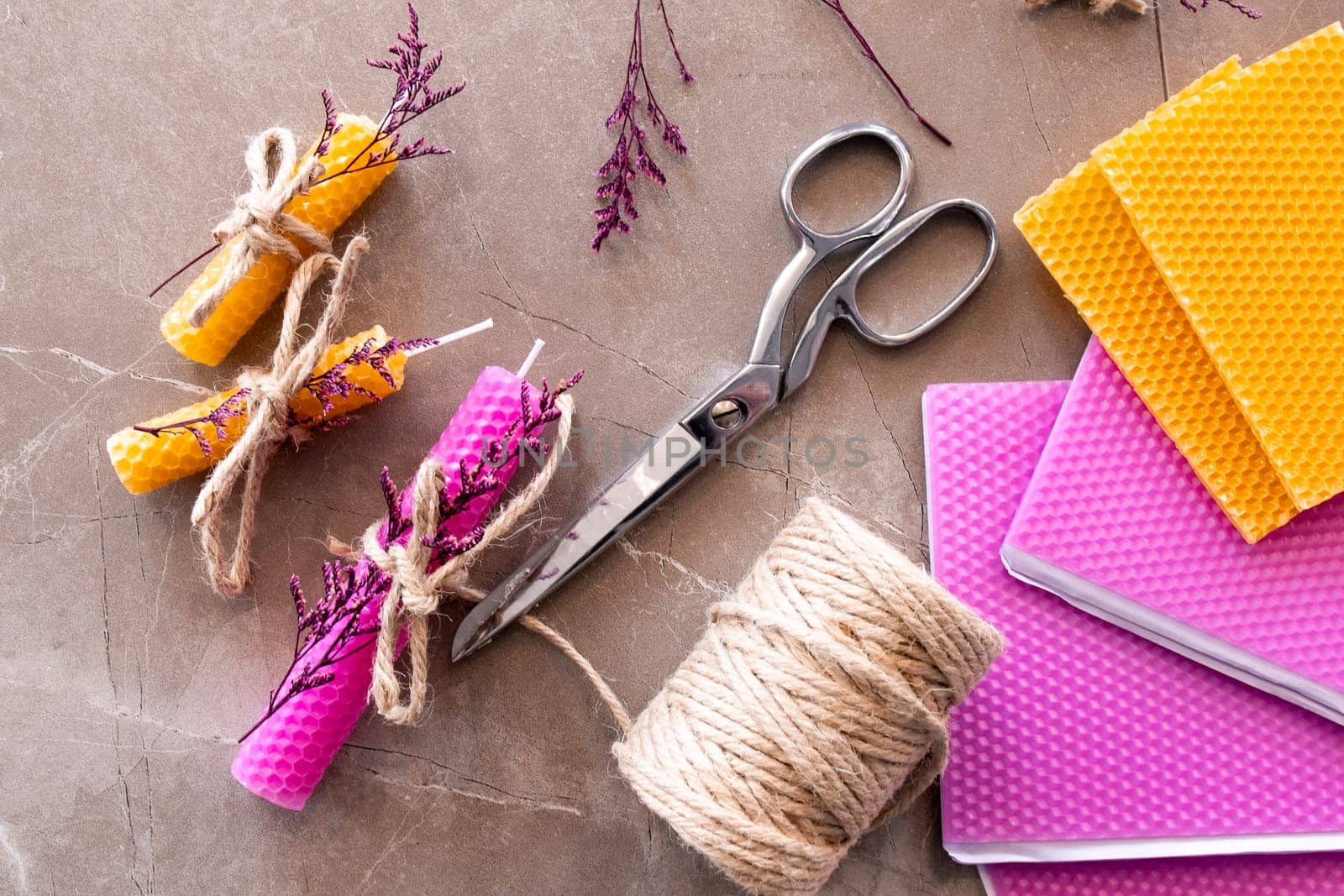 Colorful beeswax candles and craft supplies on marble surface.