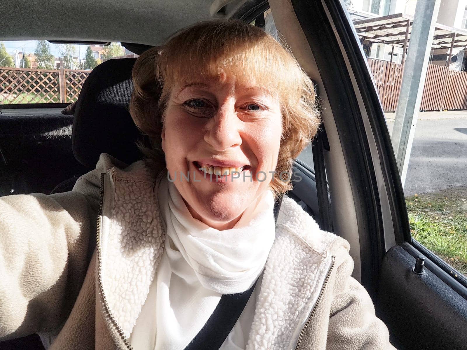 A middle-aged woman captures a lively selfie while driving on her travel excursion on a beautiful day.