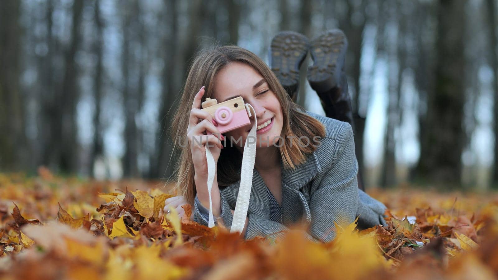 A young beautiful girl takes pictures in an autumn park using a toy camera